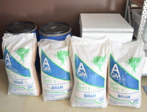 Photo of 4 20kg bags of wheat bran, two large blue storage drums and a white chest freezer. Bran is used for a commercial mealworm farm and stored in the drums. Bags of bran are placed in the freezer to kill pests.