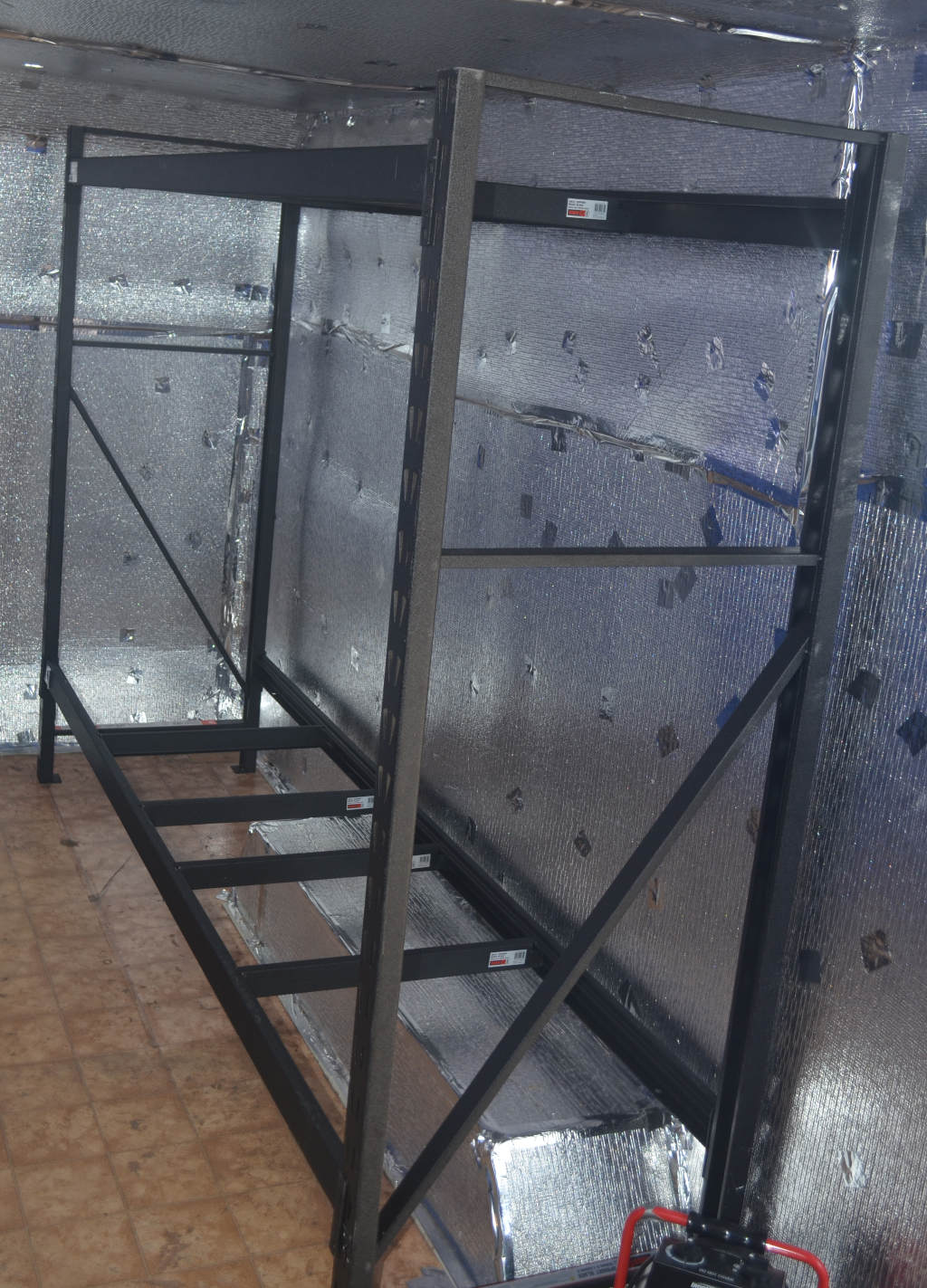 photo of a black metal frame used to make a commercial mealworm shelving. The frame sits inside a commercial insect farm with aluminium insulation on walls.